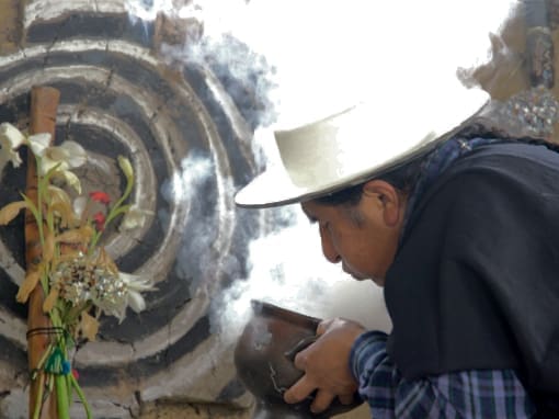 Smoke plumes rise from a ceramic bowl as a man blows into it.