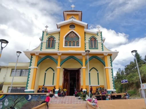 St. Luke's Church The Church of San Lucas, painted in shades of yellow with details in blue and green, with children playing on the steps and women in front of the temple preparing a festival.